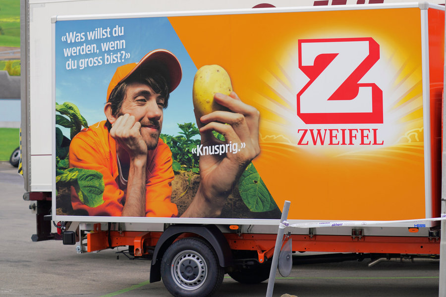 Orange Zweifel advertising trailer showing a man holding a potato and the red Zweifel logo.