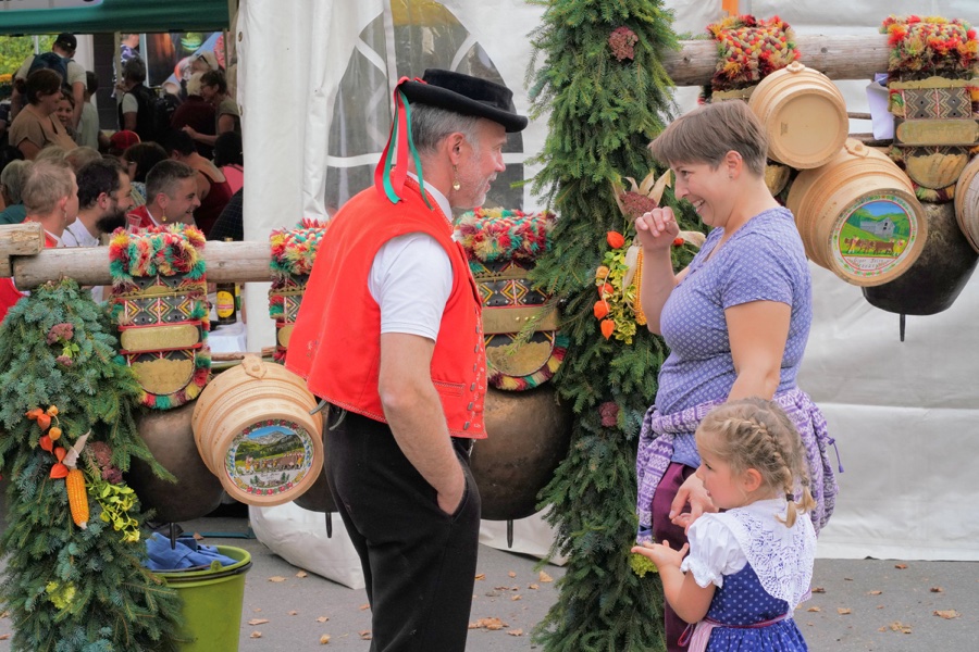 A man, a woman and a child beside large cowbells decorated with flowers.