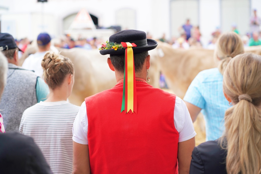 Rear view of a man wearing a red waistcoat and a black hat with colourful ribbons.