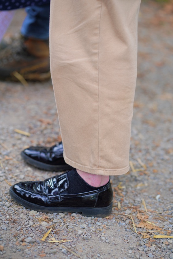 Shiny black shoes beneath beige trousers.