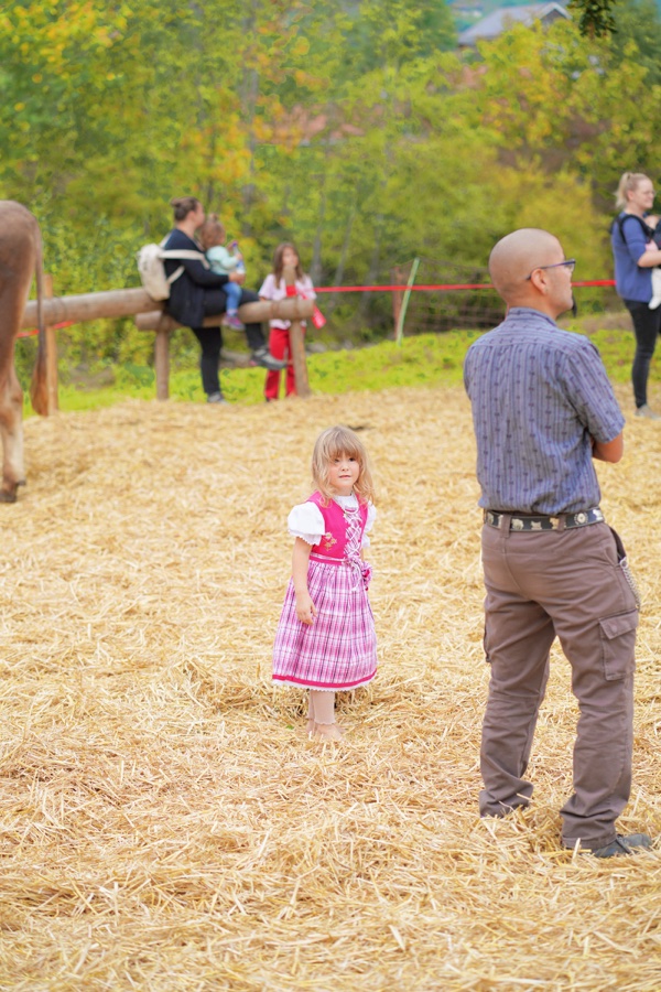 A small child in a pink dress on straw beside a man.