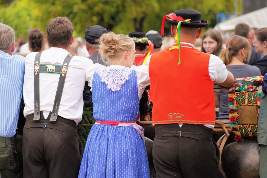 Visitors in traditional dress by a railing, including a blue dress and a red waistcoat.