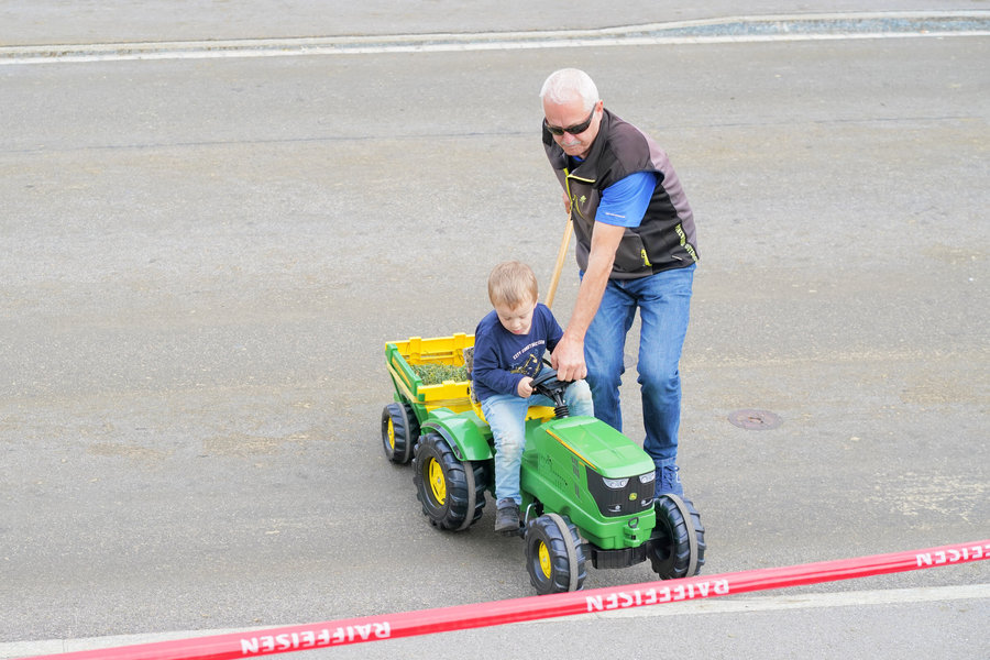 A child on a green toy tractor accompanied by a man.