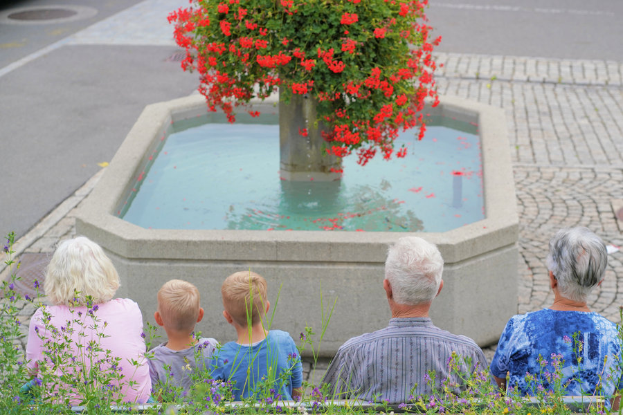 Seated spectators in front of a fountain decorated with red flowers.