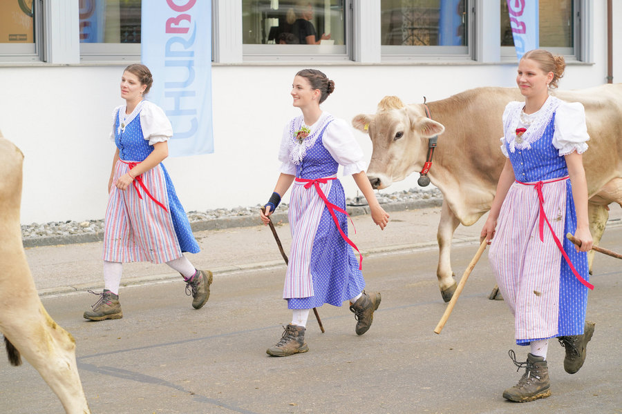 Three young women in blue traditional dress with a light-coloured cow on the village street.