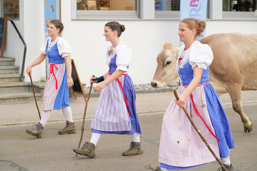 Three young women in blue traditional dress with striped skirts in front of a shop window.