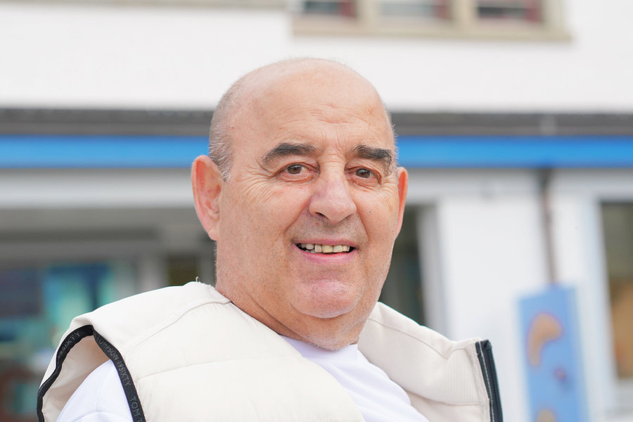A smiling man in a light-coloured quilted gilet in front of a blurred facade.