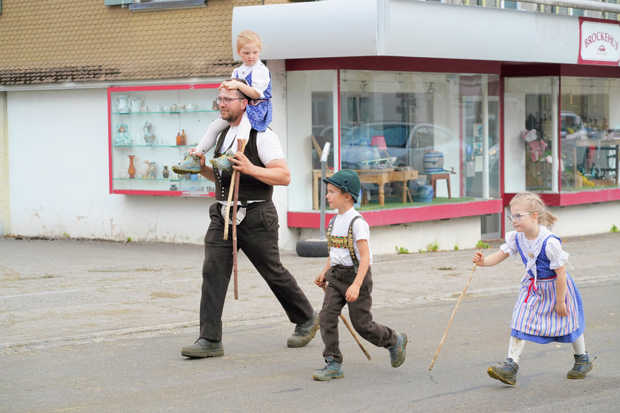 A man with a child on his shoulders and two other children in traditional dress on the village street.
