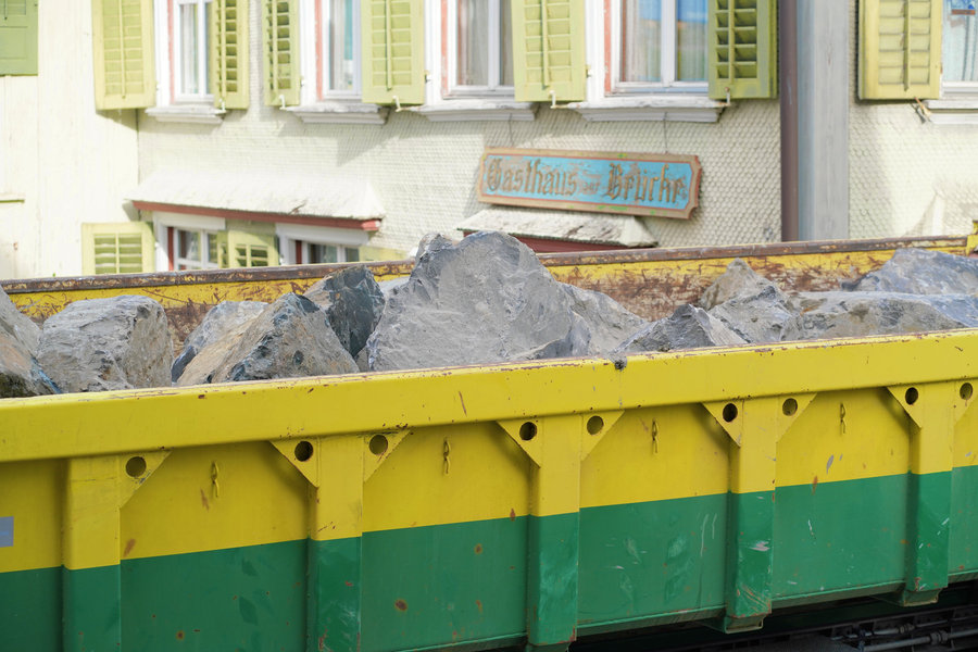A green-and-yellow trailer carrying large stones in front of the Gasthaus zur Bruecke inn.