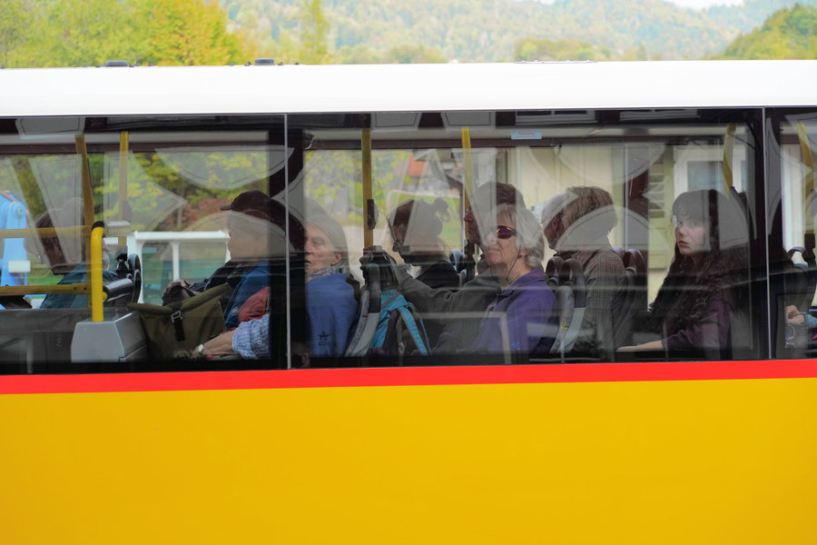 Side view of a yellow PostBus with passengers behind reflective windows.