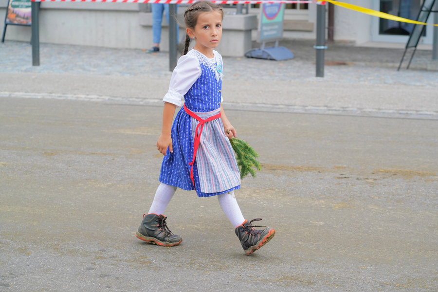A girl in blue traditional dress and white stockings takes long strides across the street.
