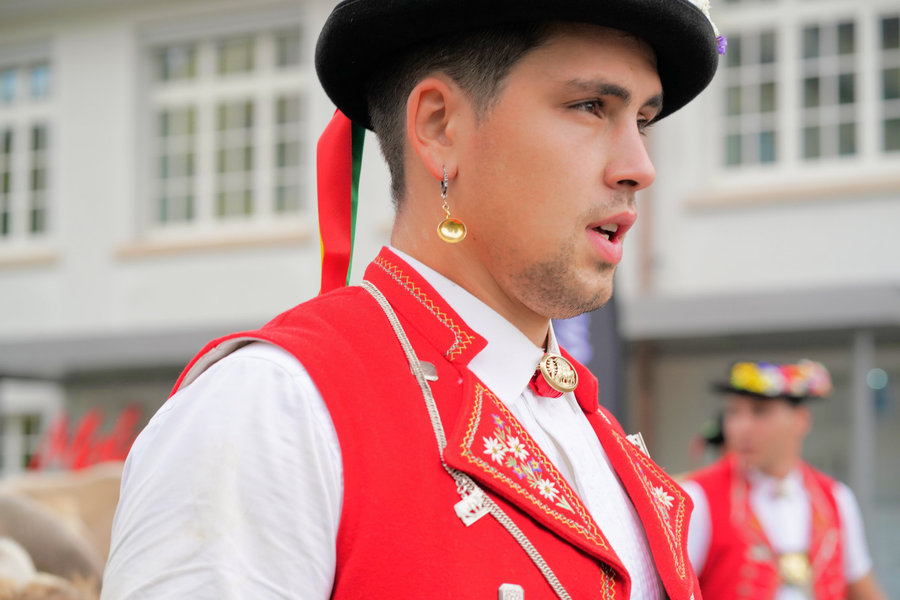 Close side view of a young man wearing a black hat, a gold earring and an embroidered red waistcoat.