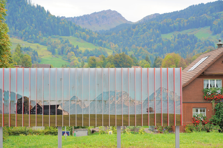 A row of narrow vertical panels displaying a mountain scene, with green slopes and a wooden house behind them.